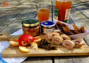 planche à découper sur laquelle se trouve : un pâté breton, un émietté de maquereau, des salicornes, une pomme en forme de crabe, des chips de sarrasin disposées dans un bateau en papier et accompagnée d'un verre de jus de pomme