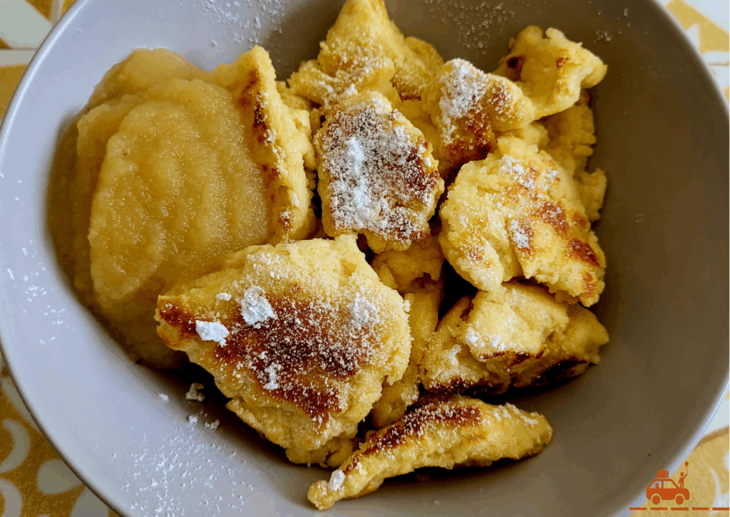 Un bol contenant des Kaiserschmarrn recouverts de sucre glace et de la compote de pommes