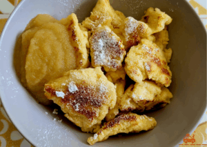 Un bol contenant des Kaiserschmarrn recouverts de sucre glace et de la compote de pommes