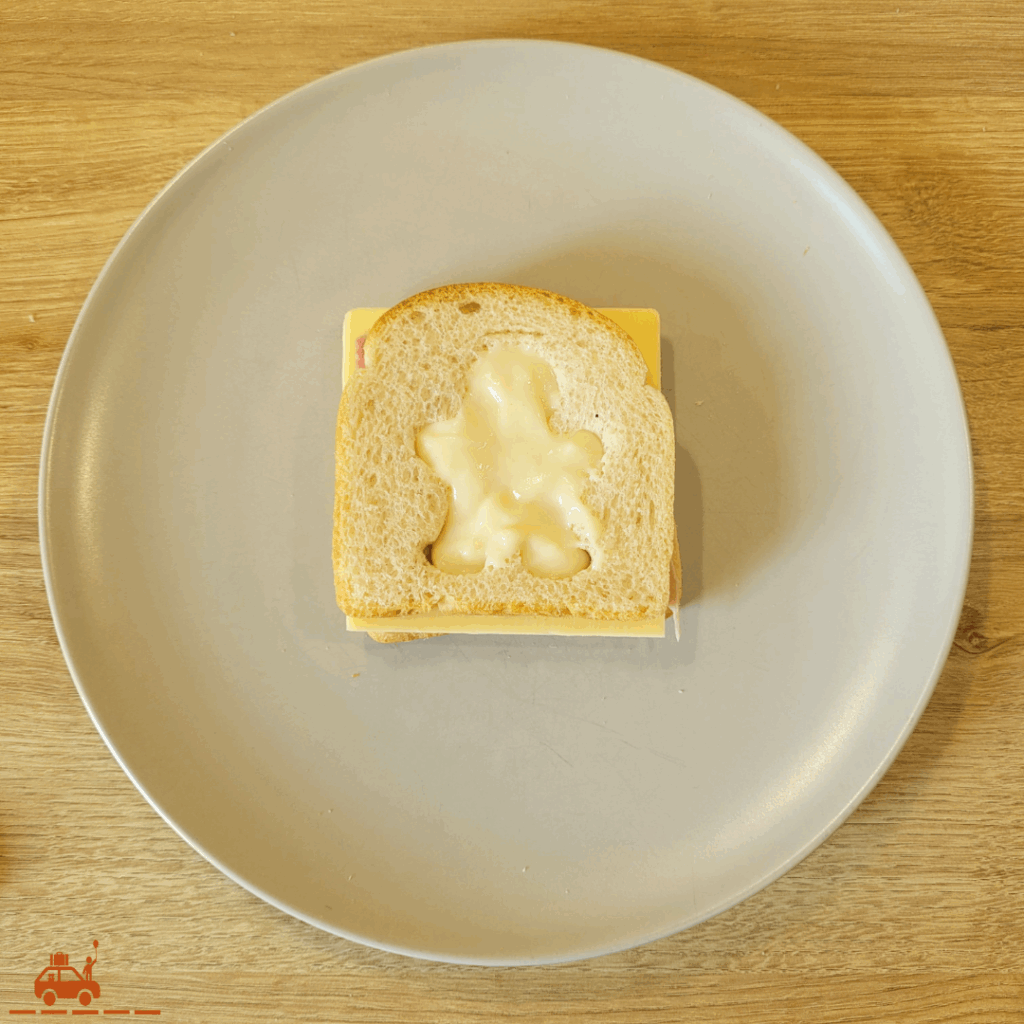 Une assiette grise contenant un croque-monsieur assemblé mais pas encore cuit avec un motif de bonhomme taillé sur le dessus