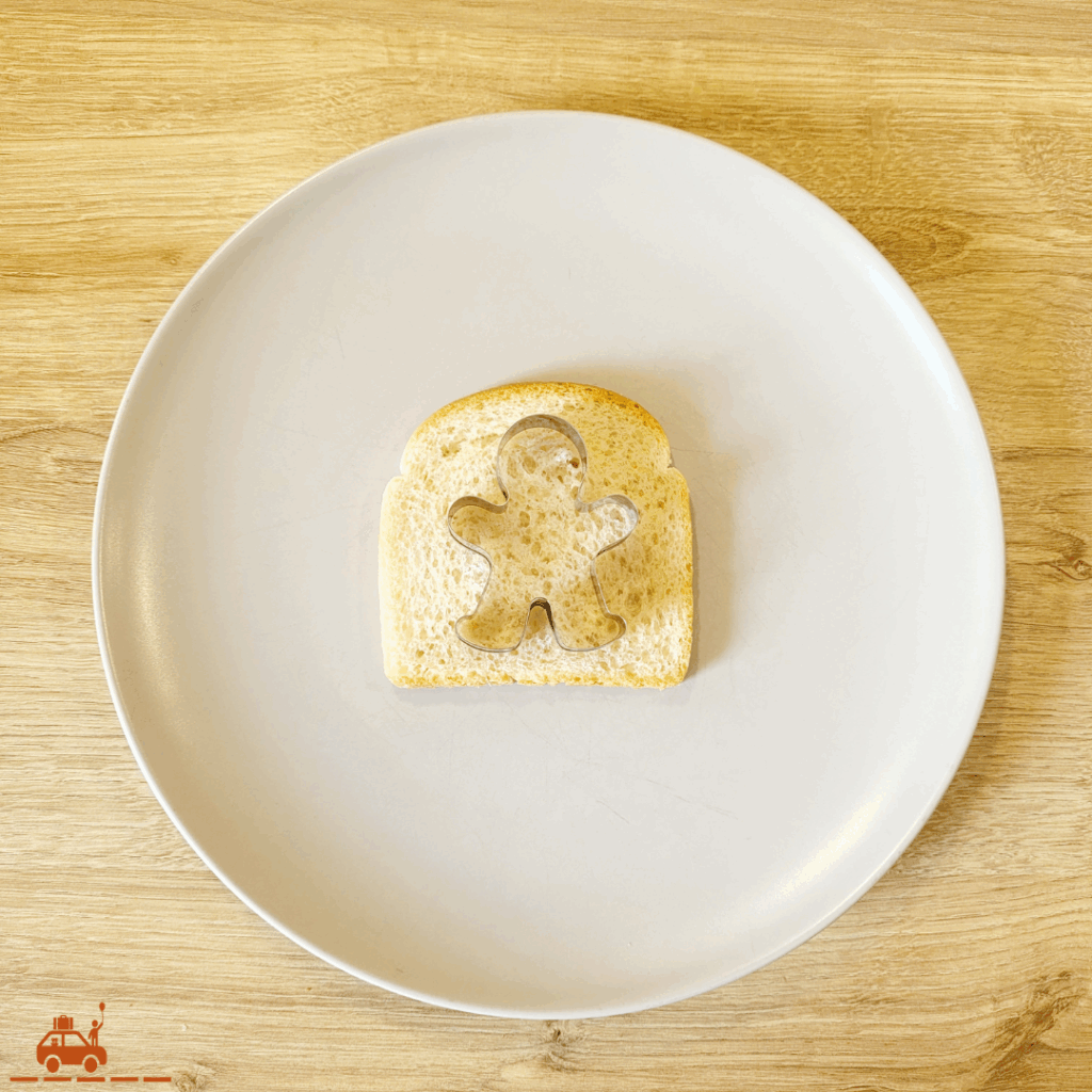 Une assiette grise contenant une tranche de pain de mie avec un emporte-pièce en forme de bonhomme posé dessus