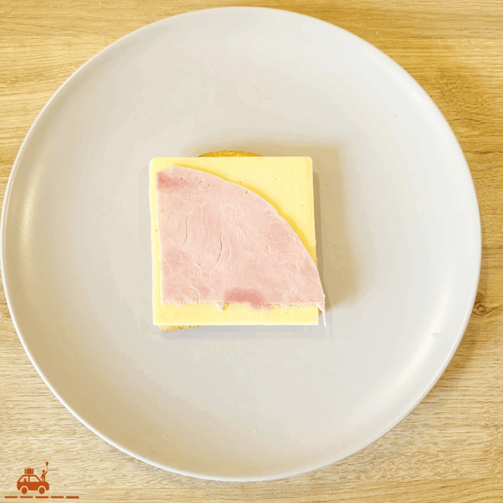 Une assiette grise contenant une tranche de pain de mie recouverte d'une tranche de fromage et d'un morceau de jambon