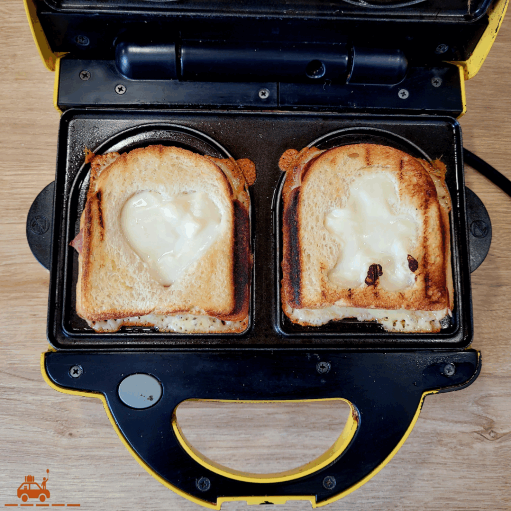 Un appareil à croque monsieur contenant 2 croques monsieur dorés et bien cuits avec des formes rigolotes (cœur et bonhomme au milieu).
