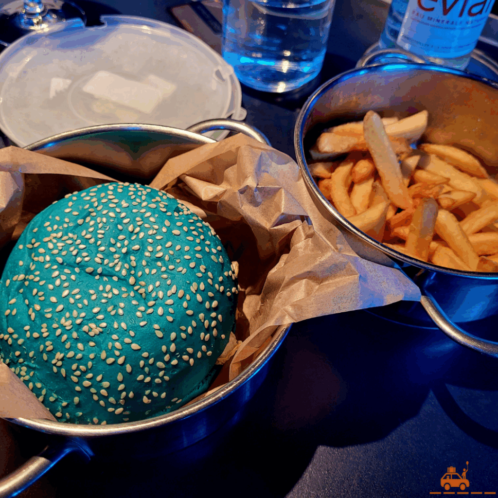 Une cassolette contenant un hamburger de couleur bleue et une autre cassolette en inox contenant des frites.