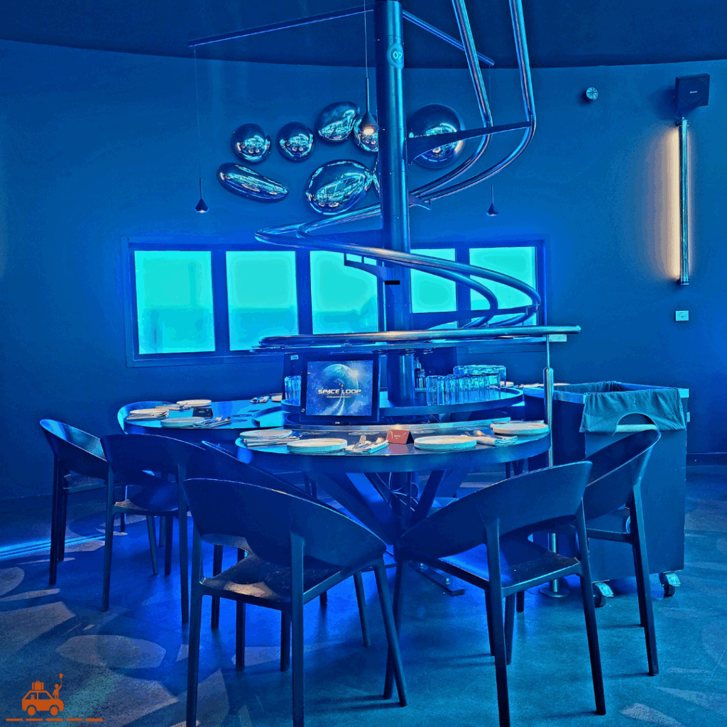 2 tables du restaurant Space Loop disposées autour d'un plateau tournant. Au-dessus du plateau, les rails où circulent les plats. En bout de circuit : la poubelle.