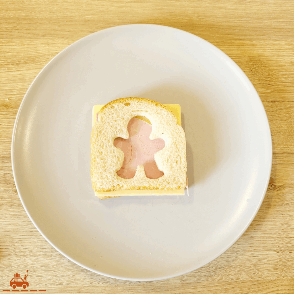 Une assiette grise contenant un croque-monsieur préparé mais pas cuit, taillé à l'emporte-pièce en forme de bonhomme.