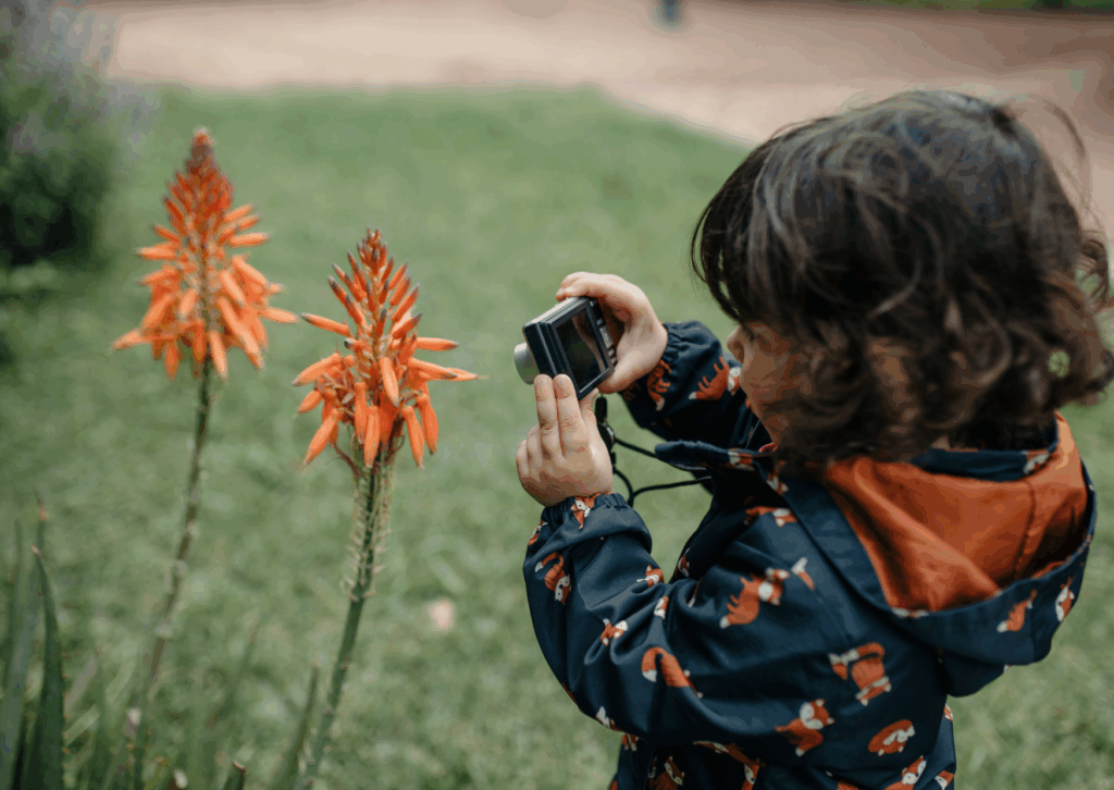 Enfant qui prend en photo des fleurs avec un petit appareil au cours d'une randonnée
