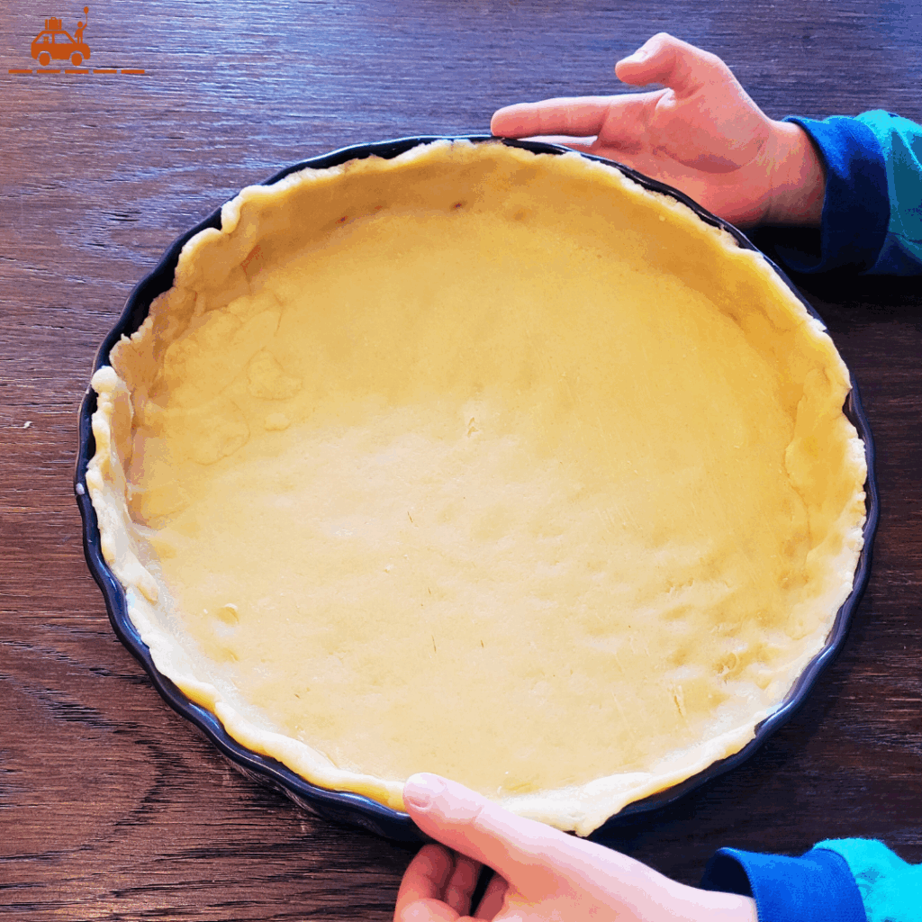 un enfant qui étale une pâte brisée dans un plat à tarte pour faire une tarte aux myrtilles