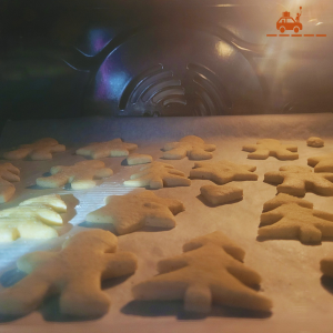 Four contenant des sablés de Noël de type bredele alsacien au beurre en train de cuire. Biscuits traditionnels en forme de sapins, bonshommes et étoiles.