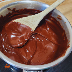 une casserole contenant du chocolat fondu mélangé avec du beurre et une cuillère en bois