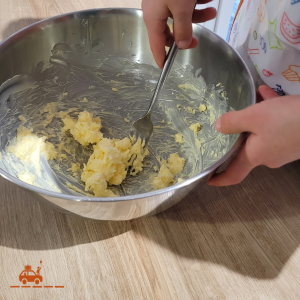 main d'enfant en train de mélanger du beurre pommade et du sucre dans un saladier avec une fourchette pour faire une pâte à Spritz (pâte à sablés viennois)
