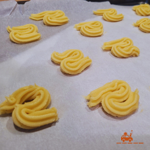 la pâte à biscuit est déposée sur une plaque recouverte de papier cuisson à l'aide d'une poche à douille cannelée afin de lui donner une forme de vague