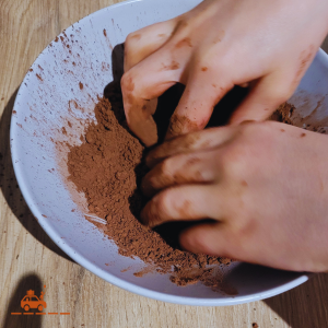 mains d'un enfant en train de préparer des truffes au chocolat maison : étape où il faut enrober les truffes de cacao en poudre.