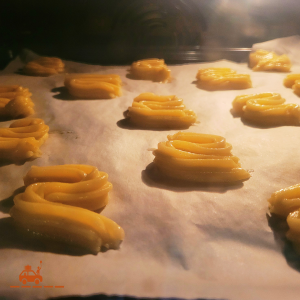 Biscuits Spritz maison en train de cuire au four sur une plaque recouverte de papier cuisson