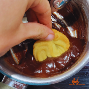 main d'enfant en train de tremper la moitié du biscuit Spritz dans la casserole de chocolat fondu pour obtenir un biscuit bicolore vanille et chocolat