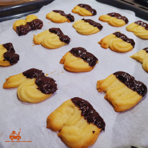 biscuits Spritz nappés au chocolat maison en train de refroidir sur une plaque de four recouverte de papier cuisson