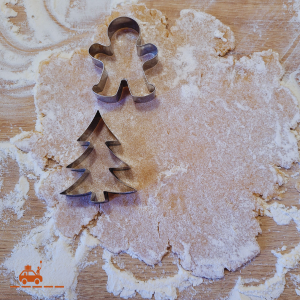 Une pâte à sablés étalée sur un plan de travail fariné et 2 emporte-pièces : un emporte-pièce en forme de sapin de Noël et un emporte-pièce en forme de bonhomme. 