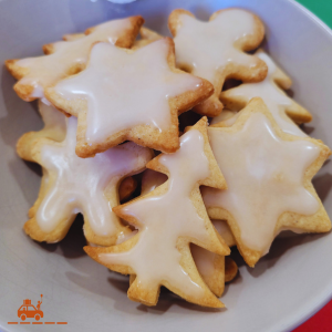 Un bol gris contenant des sablés de Noël en forme de sapins, bonshommes et étoiles recouverts d'un glaçage blanc : une recette traditionnelle alsacienne de bredele à la cannelle.