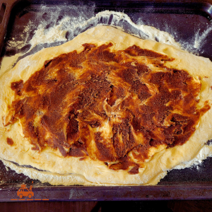 Pâte à brioche étalée sur une plaque farinée et tartinée d'un mélange de sucre, beurre et cannelle afin de réaliser des roulés à la cannelle