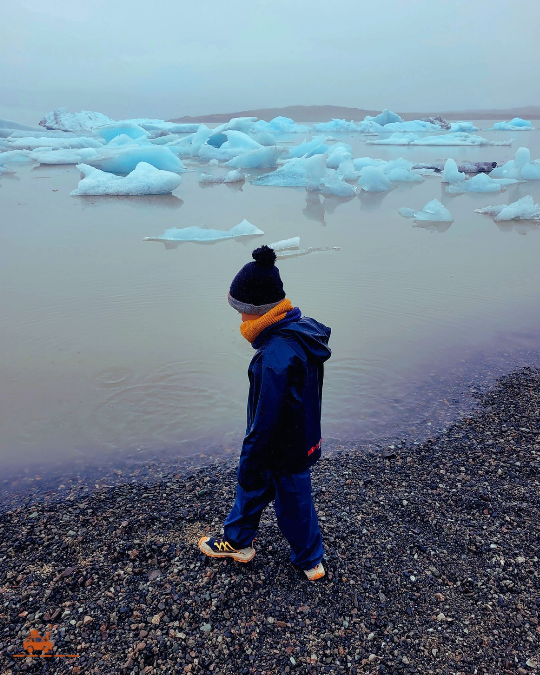 Enfant avec vêtements chauds et imperméables au bord de la lagune glaciaire de Fjallsárlón en Islande