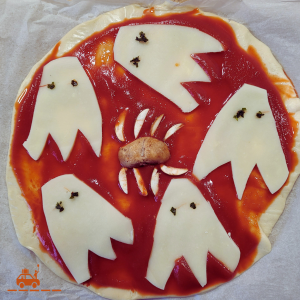 Pâte à pizza étalée avec coulis de tomate, tranches de mozzarella découpées en fantômes et champignon découpé en araignée